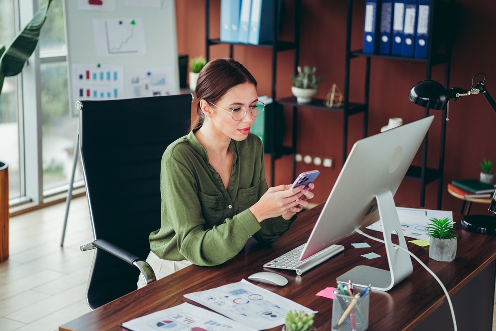 A,Focused,Young,Professional,Woman,Uses,Her,Smartphone,And,Desktop